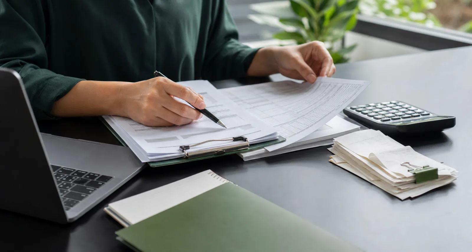 An accountant reviewing organised business records with a calculator and laptop